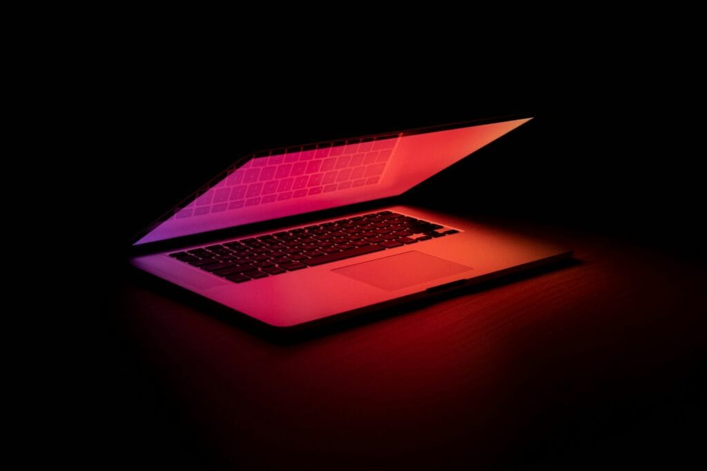 macbook pro on a wooden table. The background is dark, but there is a deep red light on the computer.